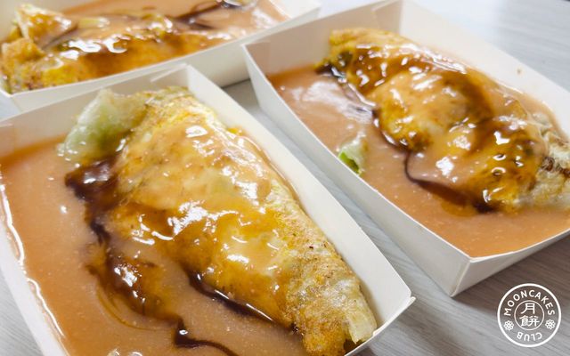 Three rectangular paper plates with oyster omlettes on them. Sauce and vegetables are visible.